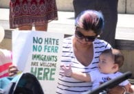A woman sits holding a baby and a protest sign