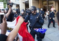 Police officer in riot gear holding back protesters