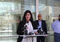 A woman at a podium speaks into microphones