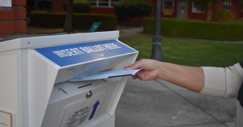A hand putting a mail-in ballot in a secure drop box
