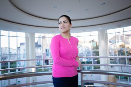 A woman in a pink long-sleeve shirt stands inside a government building