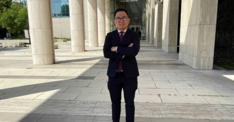 A man in a suit stands outside, with columns in the background