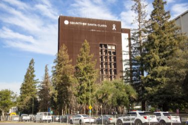 The Santa Clara County Government Center, with trees and cars in a parking lot in the foreground