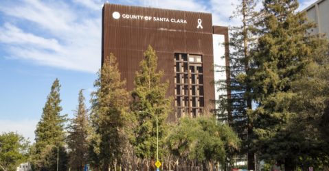 The Santa Clara County Government Center, with trees and cars in a parking lot in the foreground