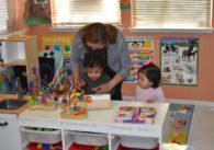 A day care worker plays with two children at a table