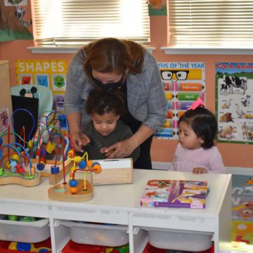 A day care worker plays with two children at a table