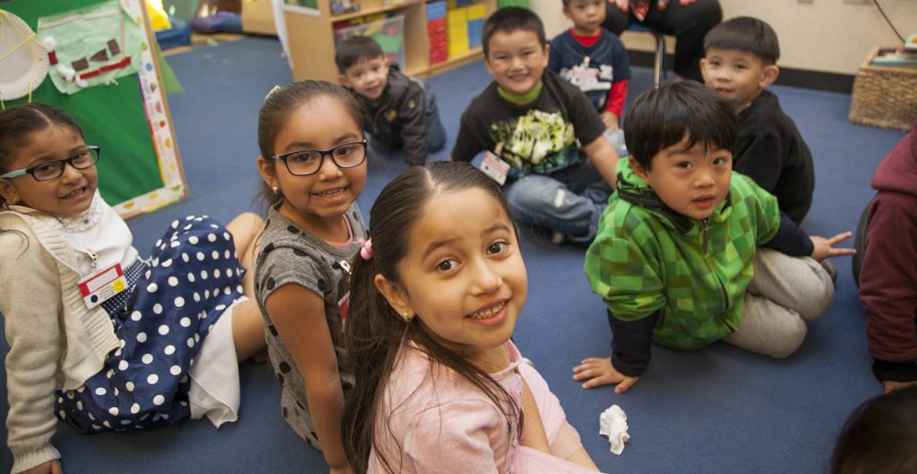 Một nhóm trẻ em đang ngồi trên sàn lớp học.