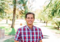 A man stands outside with trees in the background