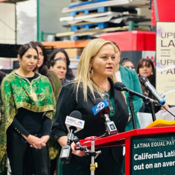 A woman stands speaking at a podium with other women behind her