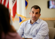 A man sitting in a chair with a flag in the background