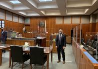 A man in a suit stands in a courtroom looking at the camera