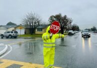 A crossing guard holding a stop sign in a crosswalk on a rainy day