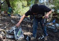 A man sorts through discarded tools and trash on the ground