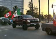 A line of trucks driving down the street carrying the Mexican flag