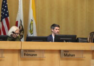 A man and woman sit behind a dais at a government meeting