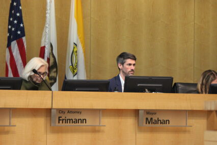 A man and woman sit behind a dais at a government meeting