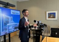 A man speaks into microphones at a podium