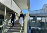 Two people walking down the stairs in the courtyard of a school with construction fencing in the background.