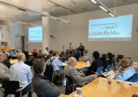Crowd of people sit at tables in front of a speaker at the Podcar City 2023 conference.