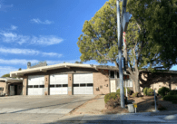 One story fire station building with three large garage doors all closed and big tree in front