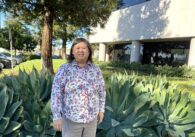 Woman (Buu Thai) standing in front of foliage and building