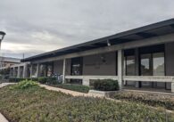 An exterior of an office building with the title Cupertino City Hall written on the front, behind green bushes.