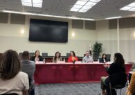 Interior of a room with a panel of people sitting at a table before an audience