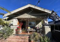 A housefront porch with an exercise bike, dresser filled with shoes, a Black Lives Matter flag and Christmas lights strung up.