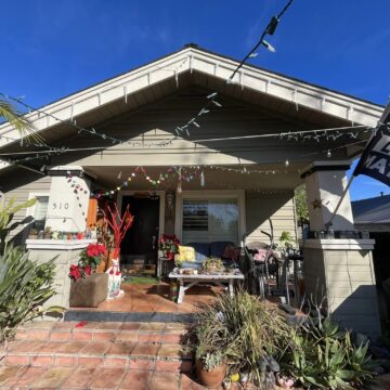 A housefront porch with an exercise bike, dresser filled with shoes, a Black Lives Matter flag and Christmas lights strung up.