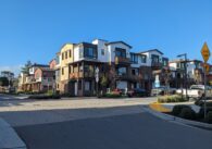 Two story modern homes along a paved street with a blue sky.