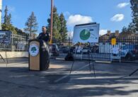 A police chief stands in front of a wooden podium with a microphone in a parking lot.