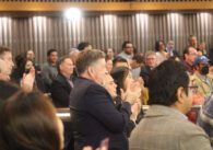 A crowd standing and clapping inside a government meeting chamber.