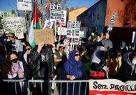 Protesters hold signs outside behind a barricade.