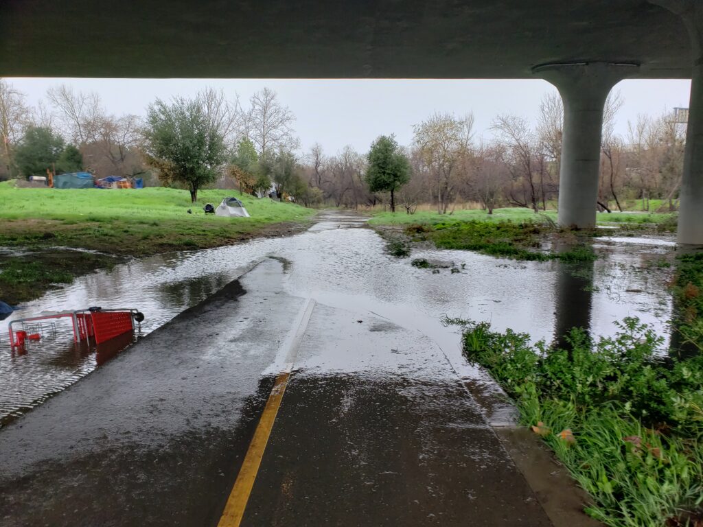 Water floods over a walkway under a bridge.