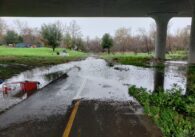 Water floods over a walkway under a bridge.
