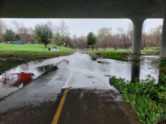 Water floods over a walkway under a bridge.