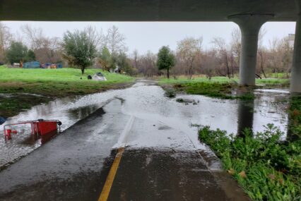 Water floods over a walkway under a bridge.