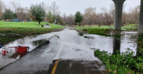 Water floods over a walkway under a bridge.
