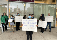 Group of people holding signs in front of San Jose City Hall, front sign reading "Why doesn't the city/county care about children?"