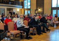 A large audience of seniors sit in an auditorium in chairs.