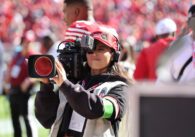A woman holds a professional video camera at a football game