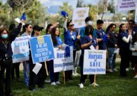 Nurses standing in their scrubs holding protest signs calling for better pay and working conditions