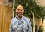 A man wearing glasses and a button down shirt stands inside