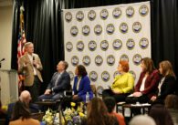 A man with a microphone speaks to a panel of people seated in chairs