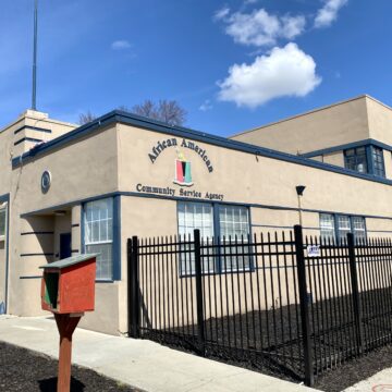 Exterior of African American Community Service Agency, beige two floor building with blue trims and black fence