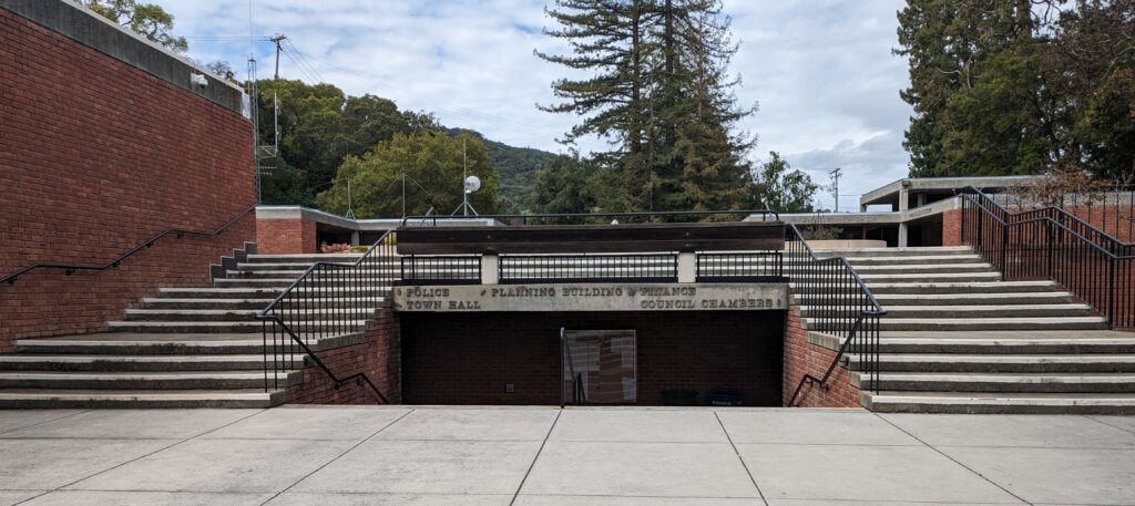 Una foto de la entrada al Ayuntamiento de Los Gatos, con escaleras que conducen a la Sala del Consejo y al Departamento de Planificación, Construcción y Finanzas, y escaleras que conducen al Departamento de Policía y al Ayuntamiento.