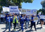 Group of striking nurses wearing blue shirts reading #RNPASTRONG and holding signs while walking across the street. Signs read "Santa Clara County Nurses for a Strong Contract", "Willing to strike for my patients", and "RNPA Protect us, Pay us, Respect us."