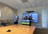 One man standing at a podium at city hall with another off to the side