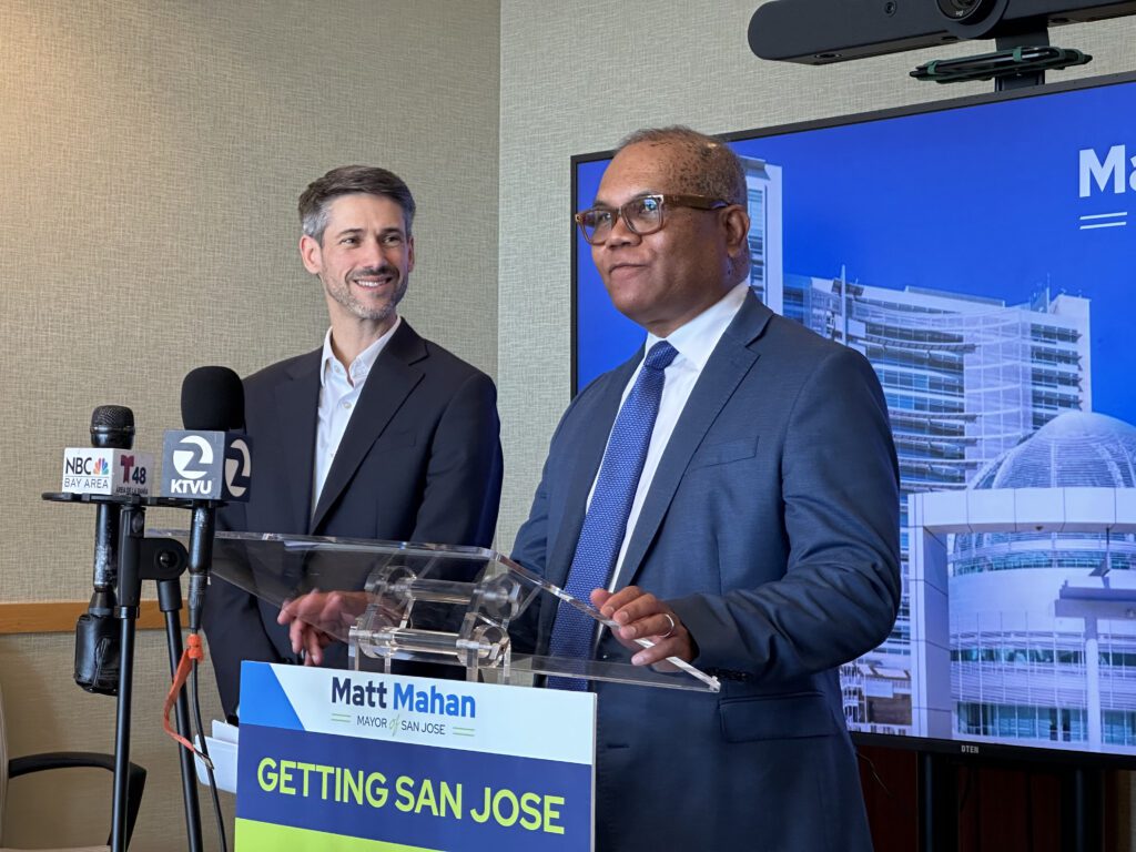 Dos hombres de pie en un podio con micrófonos en San José, California.