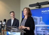 A man and woman stand inside at a podium during a press conference in San Jose